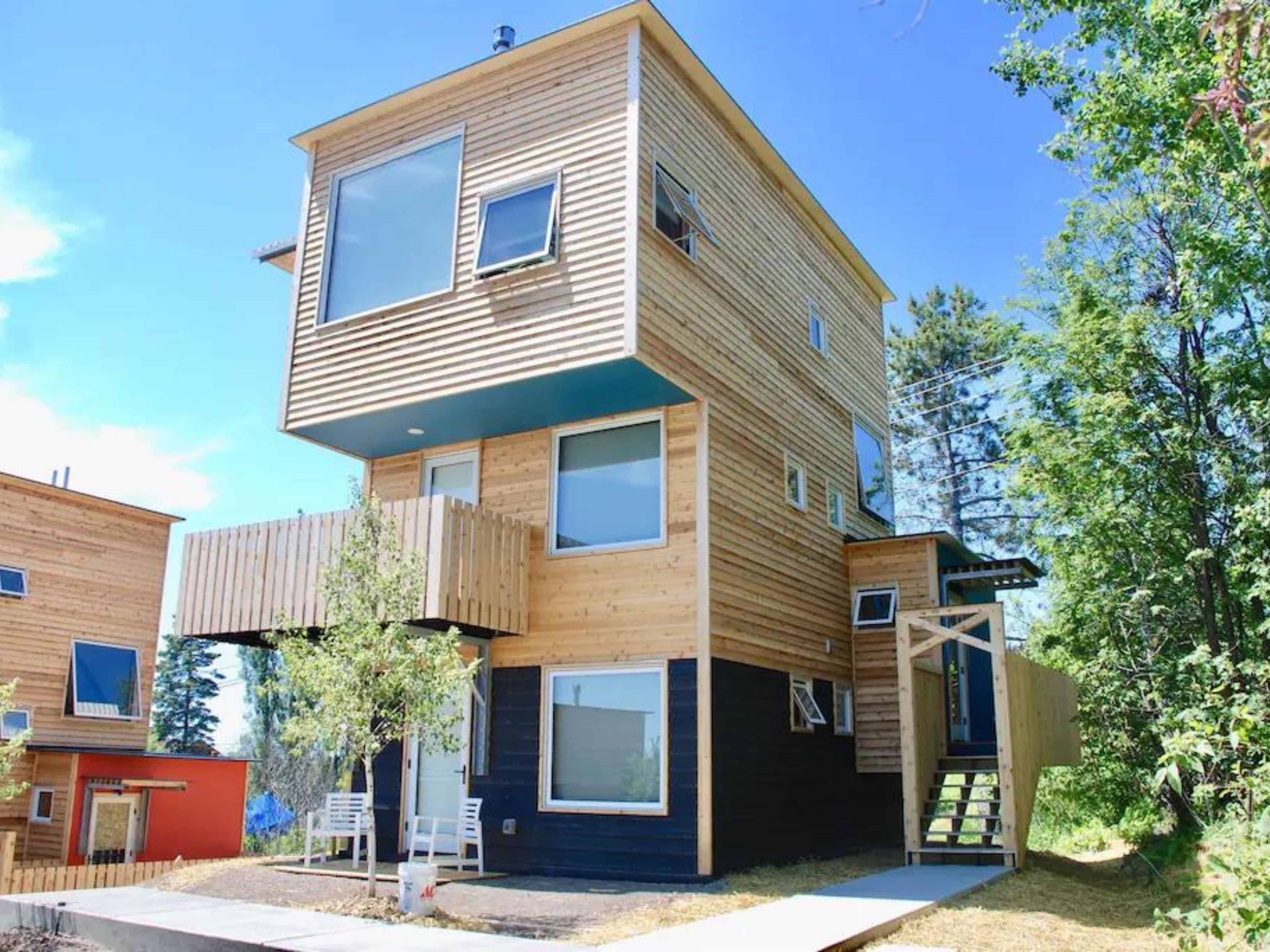 A unique shaped house with wood pallets on the outside. It is rectangle, very tall, and skinny.