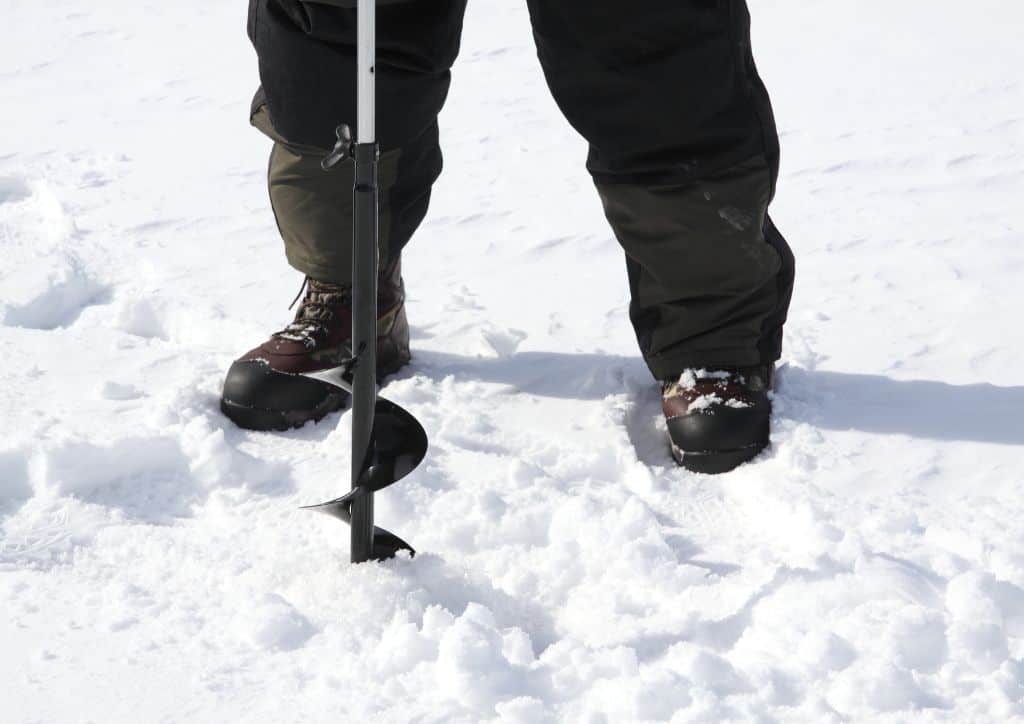 A person using an ice auger to drill a hole into the frozen lake.