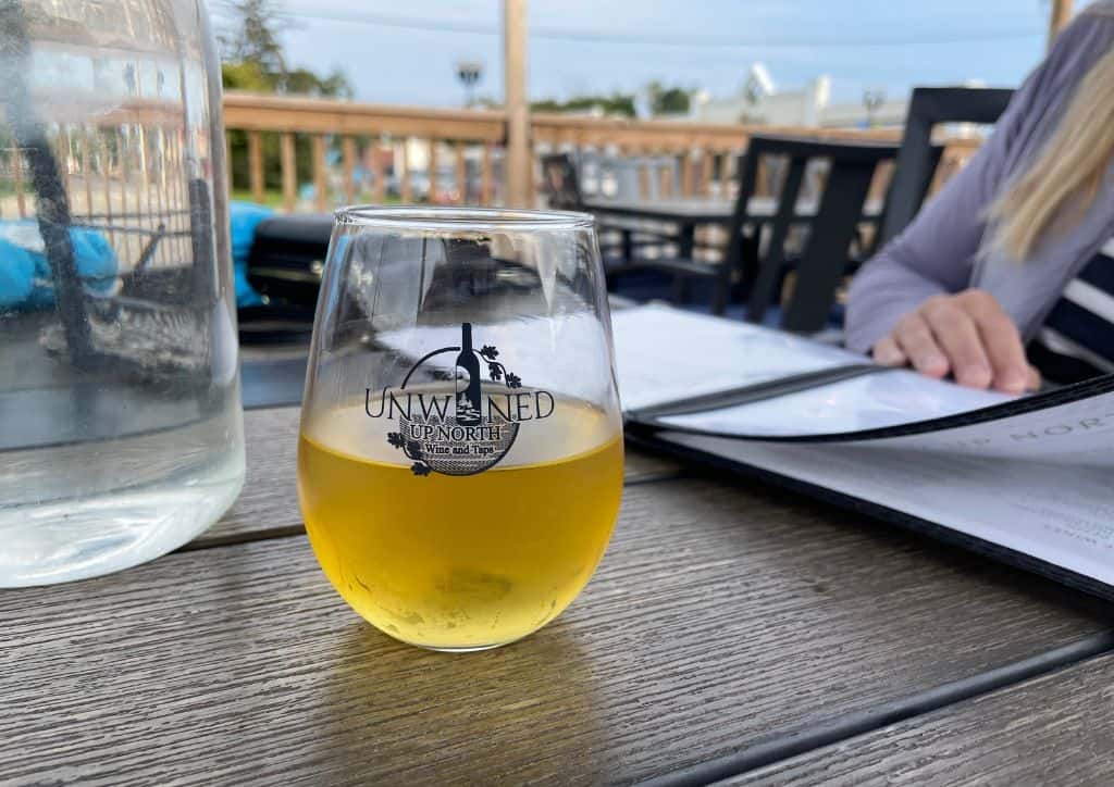 A glass of peach wine sitting on a table from Unwined Up North.
