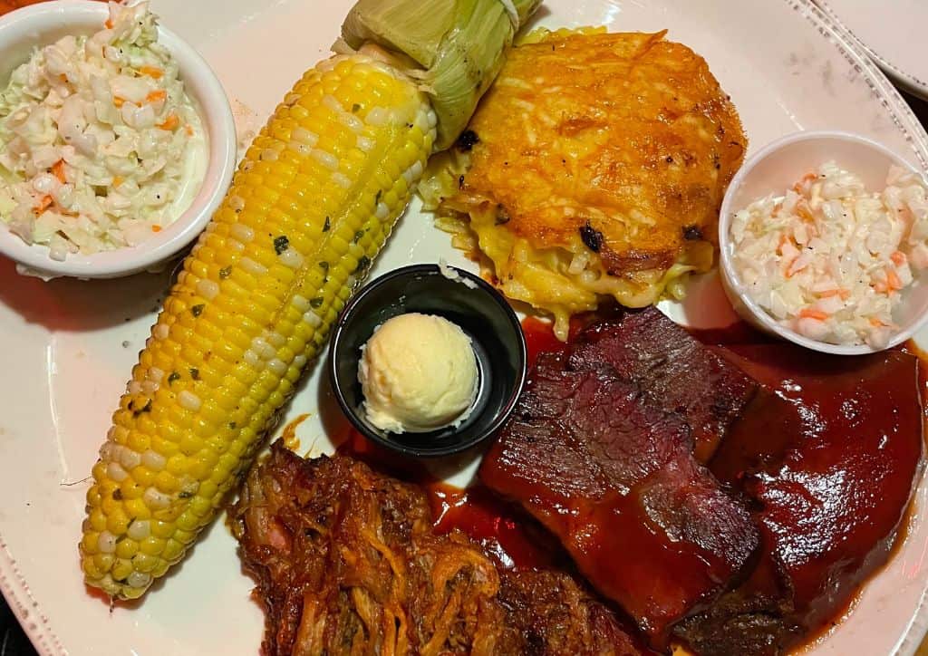 A plate of barbeque food such as corn and cheesy potatoes.