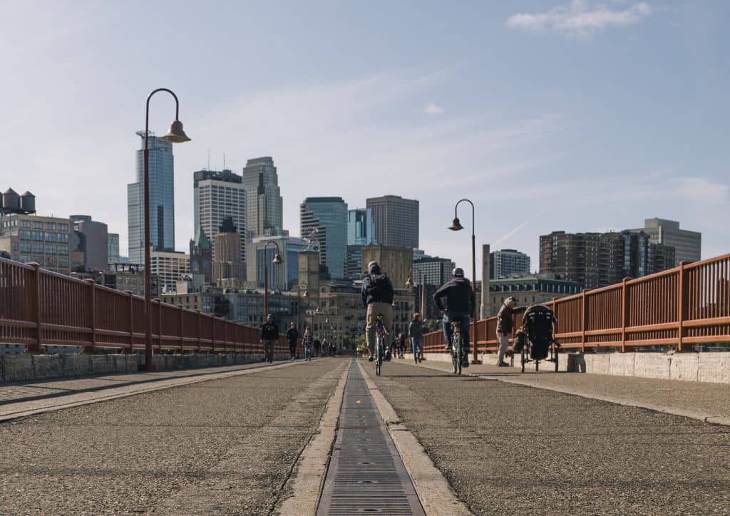 A bridge with bicyclists crossing it near skyscrapers.