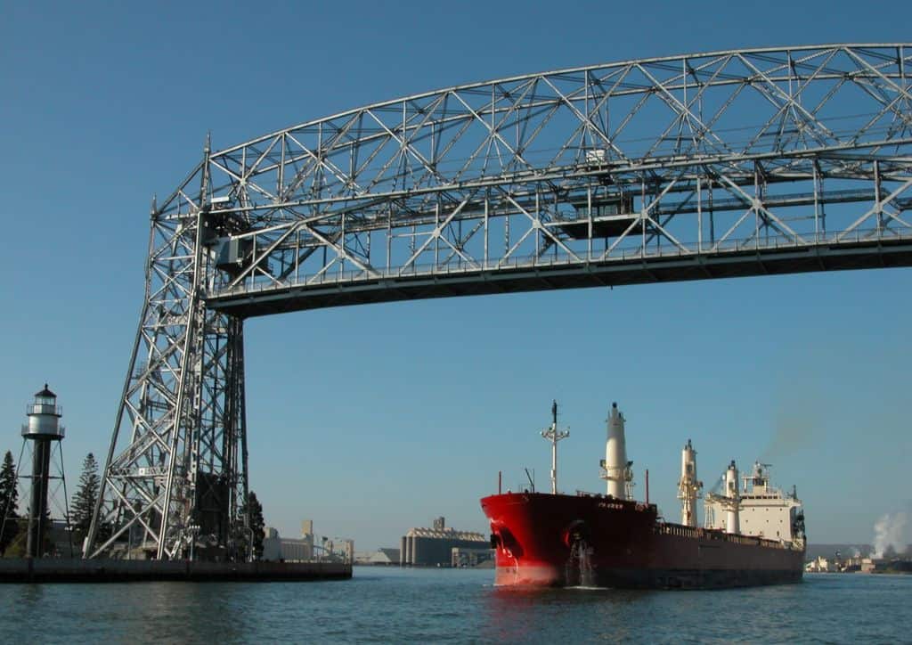 A large, red ship passing under the Aerial Lift Bridge in Duluth, MN.