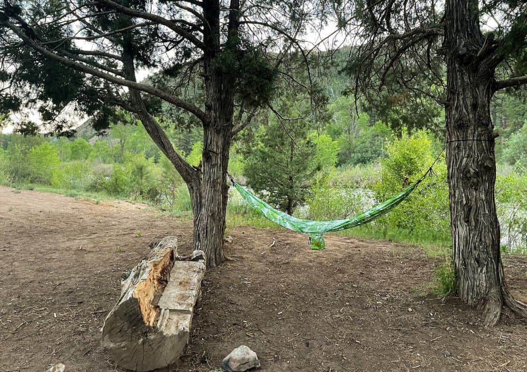 A hammock hanging from a tree by a log bench at a Minnesota camper cabin.