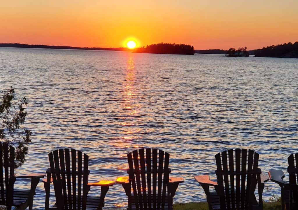 Five chairs sitting on the shore of a lake for swimming in Minnesota at sunset.
