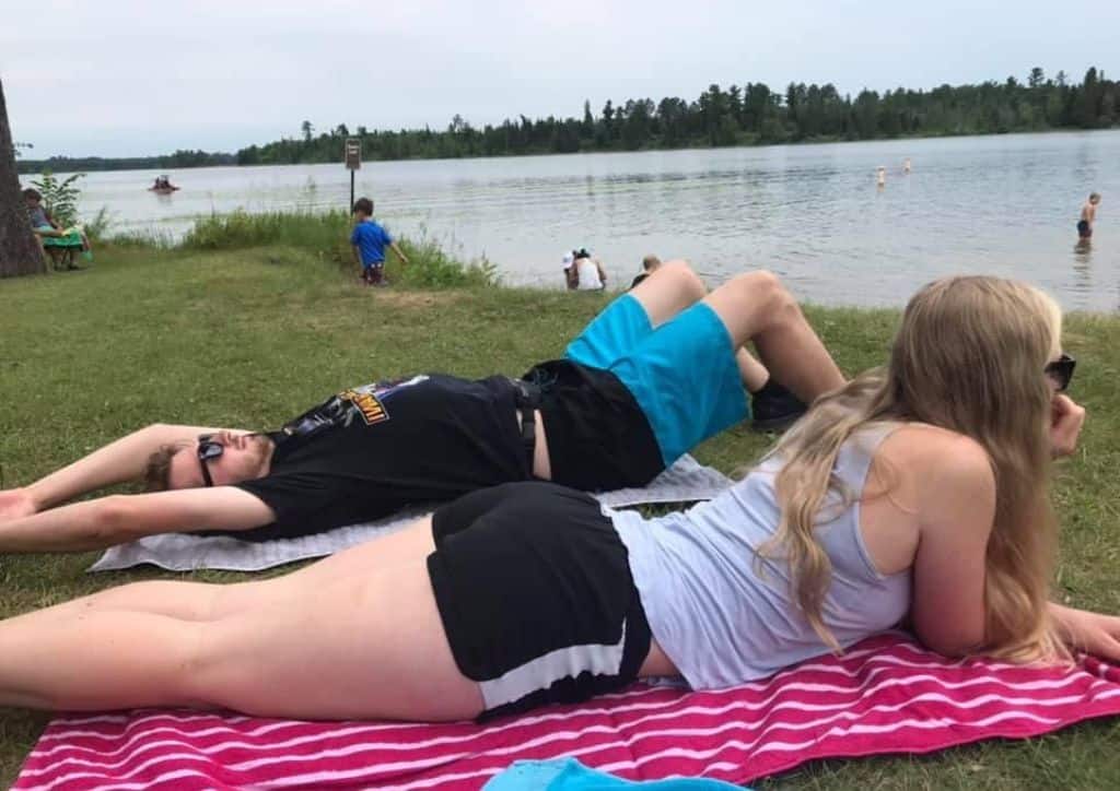 Myself and Tyler laying on a towel near Lake Itasca while people swim in Minnesota.
