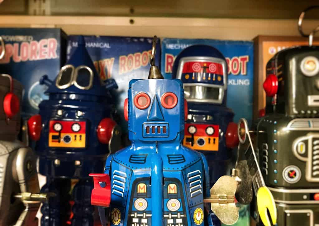 Several toy robots sitting on a shelf at an antique store.