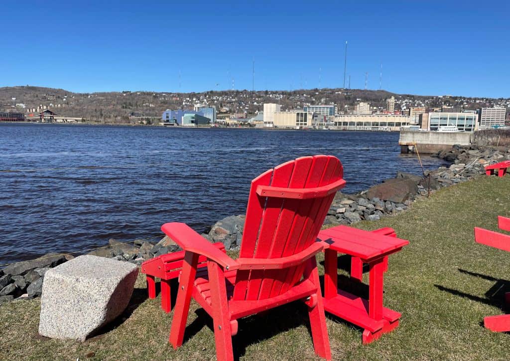A red chair sitting on the shore near a canal on Lake Superior.