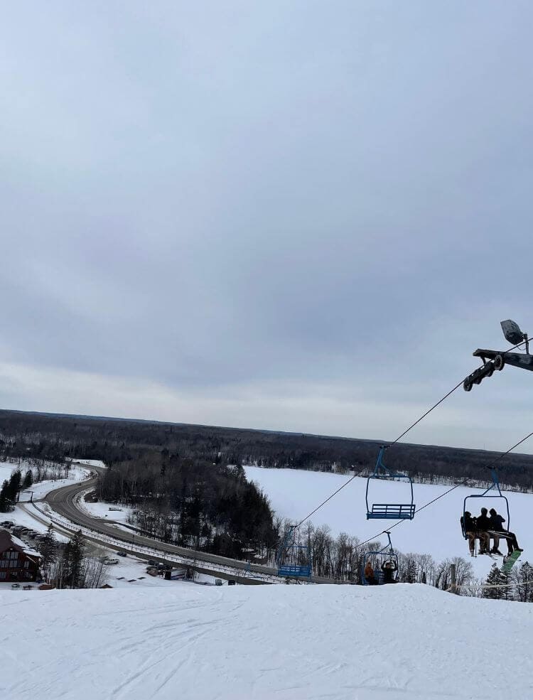 An overlook from the top of a ski hill that looks out at a lake, road, and ski lift.